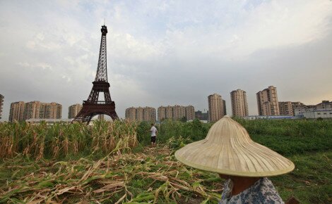 Farmer walks through field near a replica of the Eiffel Tower at the Tianducheng development in Hangzhou